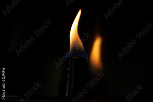 Alcohol burns on a stack for alcoholic drinks. Tongues of flame around a metal cup. Texture of fire. Yellow fire on a black background. Fire at the bar. The tradition of setting fire to alcohol.