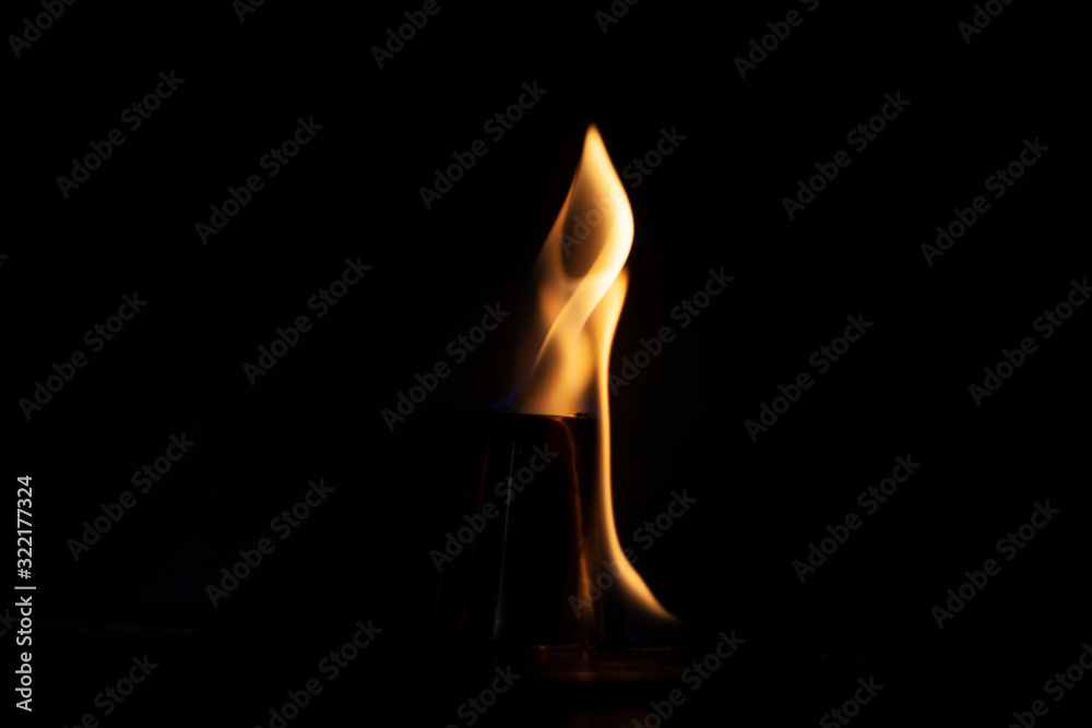Alcohol burns on a stack for alcoholic drinks. Tongues of flame around a metal cup. Texture of fire. Yellow fire on a black background. Fire at the bar. The tradition of setting fire to alcohol.