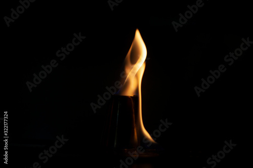 Alcohol burns on a stack for alcoholic drinks. Tongues of flame around a metal cup. Texture of fire. Yellow fire on a black background. Fire at the bar. The tradition of setting fire to alcohol.