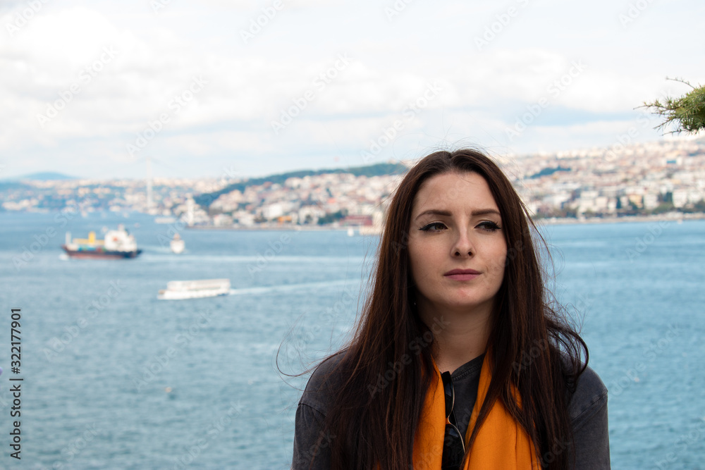 Attractive brunette with an uneasy look looking into the distance. Bosphorus canal in Istanbul, turkey behind her , blurred ships and istanbul peninsula