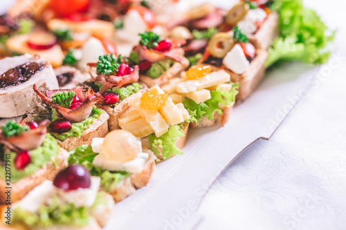 Crostini with meat, fruits, vegetables and cheese close up on table.