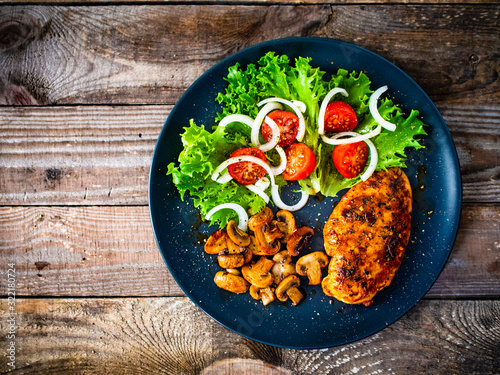 Roast chicken breast and vegetables on wooden background