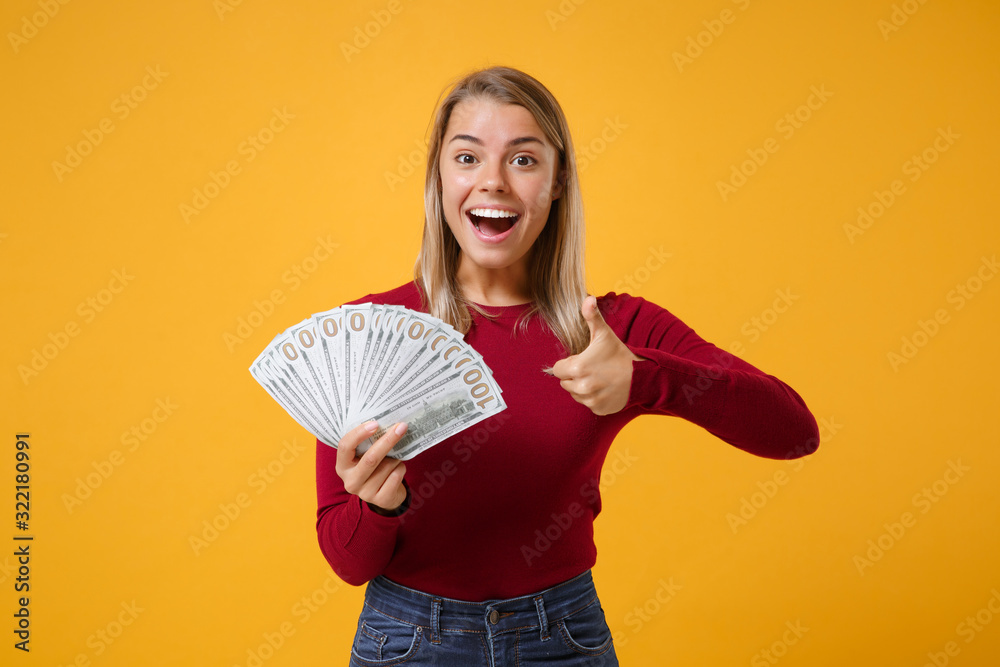 Excited young blonde woman girl in casual clothes posing isolated on yellow orange background. People lifestyle concept. Mock up copy space Hold fan of cash money in dollar banknotes showing thumb up Excited young blonde woman girl in casual clothes posing isolated on yellow orange background. People lifestyle concept. Mock up copy space Hold fan of cash money in dollar banknotes showing thumb up