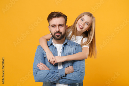 Bearded man in casual clothes have fun with cute child baby girl. Father little kid daughter isolated on yellow wall background. Love family day parenthood childhood concept. Hugging, showing tongue.