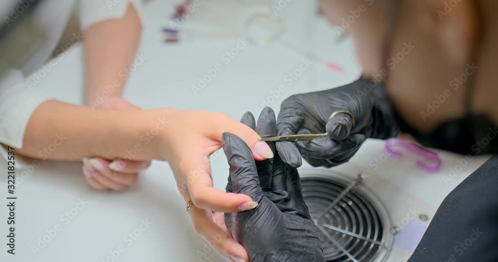 Manicurist scissors a cuticle from a client’s nail. Professional manicure in the salon of nail service. Close-up. Manicurist scissors a cuticle from a client’s nail. Professional manicure in the salon of nail service. Close-up.