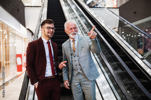 Two businessmen standing in front of escalator and talking.