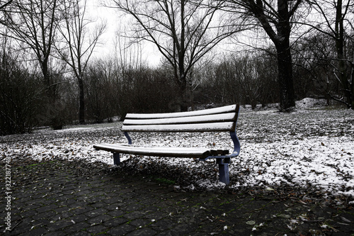 Depressing Ice cold winter mood in city park with a snow covered empty bench.