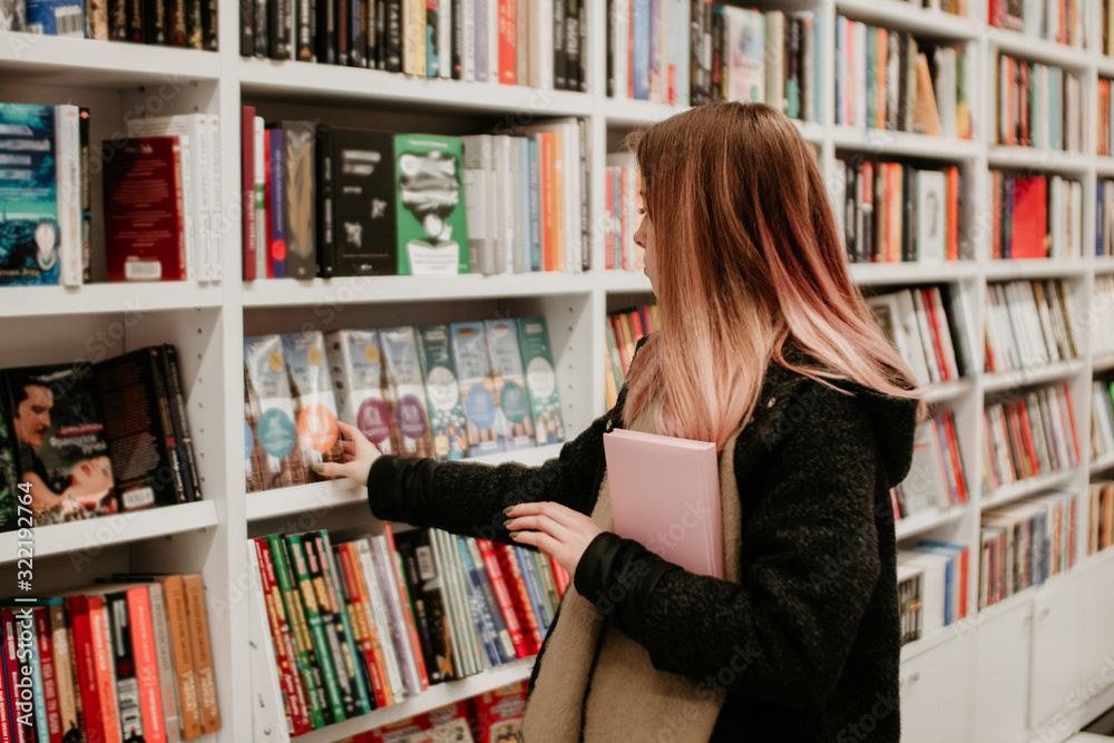 Portrait of a beautiful blonde woman looking for a book in store