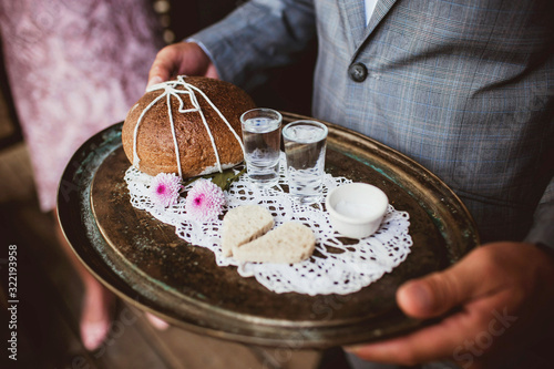 Wedding tradition in Poland and Russia. Parents welcome bride and groom with bread, vodka and salt. Decorative tray with food and alcohol. Empty copy space european culture background.