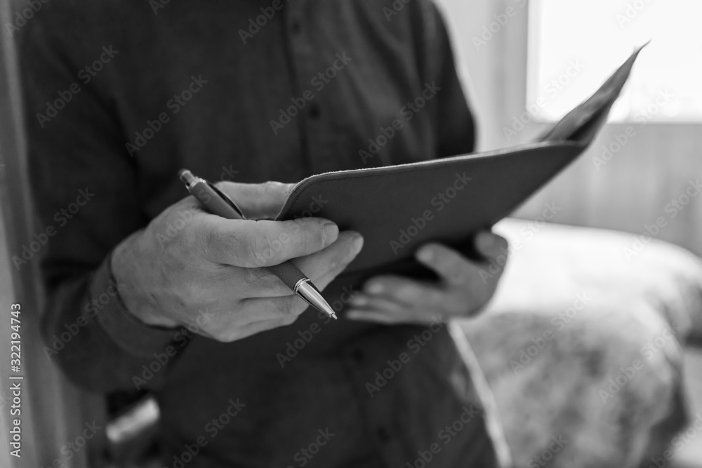 selective focus and close up view of a man's hands as he holds a notebook and pen, he is reading notes, black and white with copy space