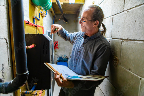 middle aged home Inspector is visiting the equipment technical room during an inspection. Caucasian man inspects plumbing and electricity with notebook photo