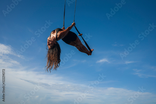 aero yoga workout - young attractive and athletic woman practicing aerial yoga exercise training acrobatic  body postures isolated on blue sky in balance flexibility control photo