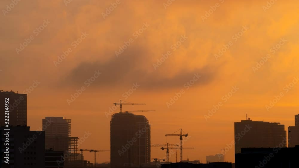 Aerial shot (TimeLapse 4K VIDEO) of city silhouette from dusk to night with flying clouds and sky color changes. In the background working cranes and skyscraper building in the process of construction Aerial shot (TimeLapse 4K VIDEO) of city silhouette from dusk to night with flying clouds and sky color changes. In the background working cranes and skyscraper building in the process of construction