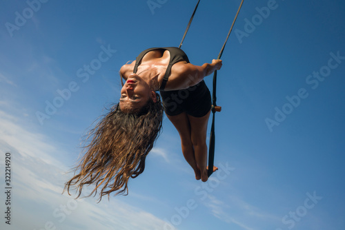 aero yoga workout - young attractive and athletic woman practicing aerial yoga exercise training acrobatic body postures isolated on blue sky in balance flexibility control