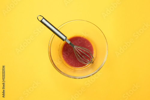 Dirty empty bowl with whisk on color background