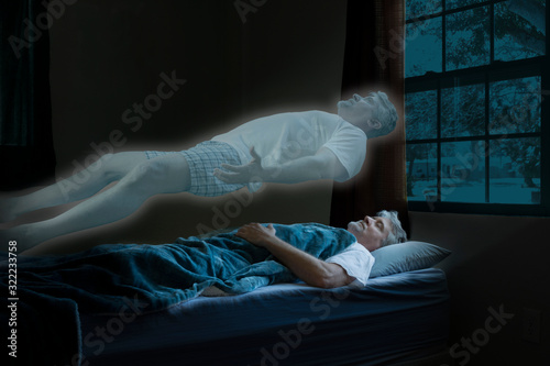 Glowing spirit or angel coming out of a dead man who has died in his sleep as it floats above him ascending into heaven as moonlight shines on the poor gentleman.
