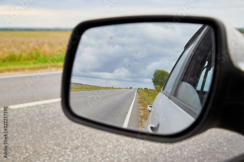 The reflection of road in the side view mirror in autumn day. Travel concept