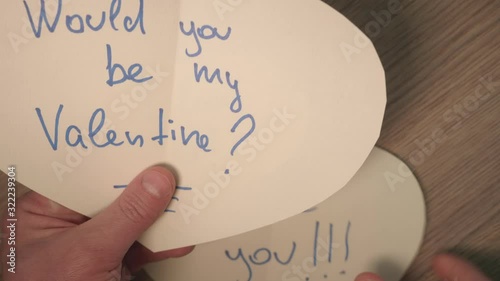 Man's hands hold several heart shaped cards from stranger with romantic writings. Up view and close up.