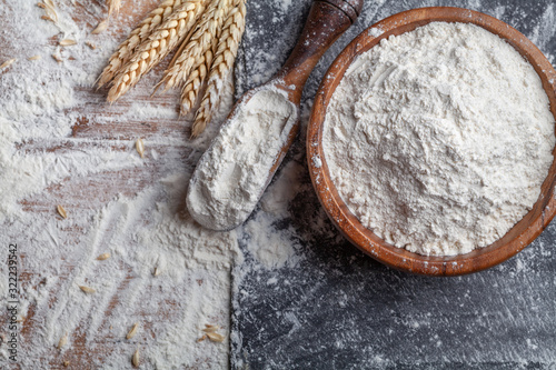 Foto Wheat flour with scoop and wheat ears on kitchen board top view