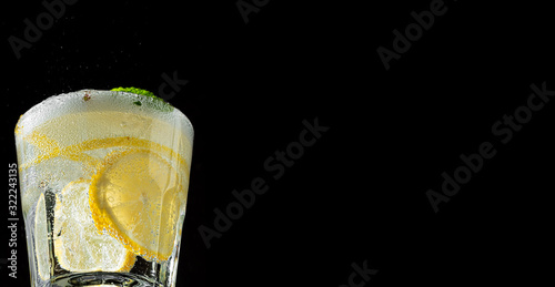 Cold drink on a black background. One glass with lemonade or mojito cocktail with lemon and mint. Close up, copy space