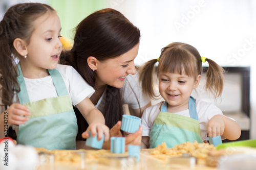 Mom and her cute kids daughters are playing and joying while baking in kitchen at home