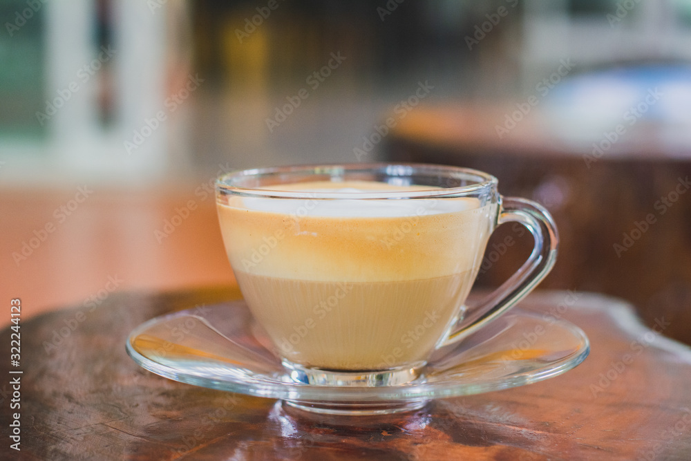 Layer of hot cappuccino coffee and milk froth in clear cup on wooden table in coffee shop. Layer of hot cappuccino coffee and milk froth in clear cup on wooden table in coffee shop.