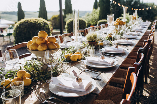 in the back yard of the old villa there is a long festive table, which is decorated with lemons and herbs, on the table are plates, glasses and candles. Wedding in Italy. Tuscany