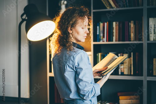 Portrait of beautiful blond woman with book on hand thinking at the library. photo