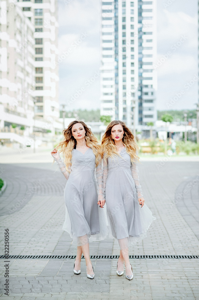 two attractive twin women in identical light dresses against the background of the city