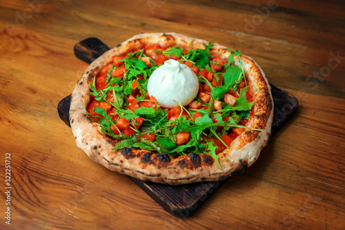 Freshly baked pizza with cheese, arugula, and burrata on a wooden table