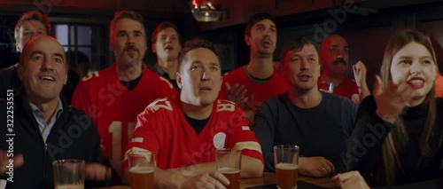 MED Model released, American football fans wearing generic red uniform watching a game on a TV in a sport pub, rooting for their team. 4K UHD, shot on ARRI Alexa Mini with Cooke S4 lenses photo