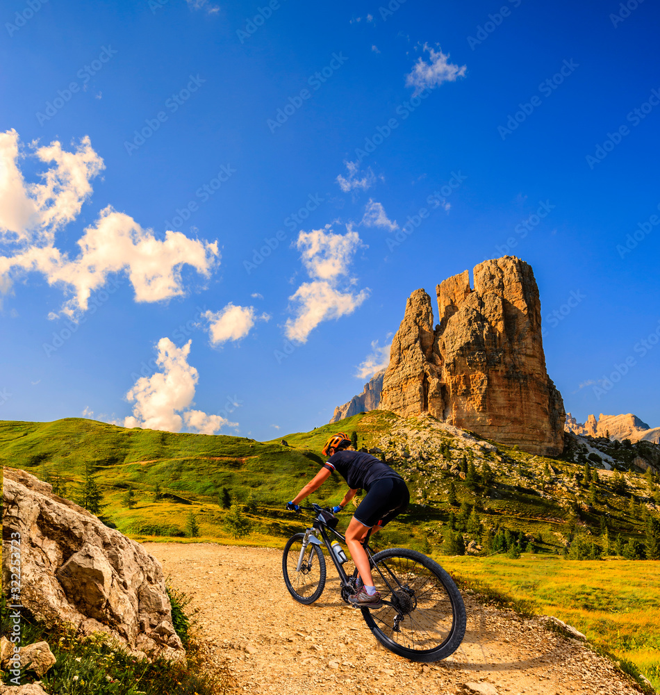 Tourist cycling in Cortina d'Ampezzo, stunning rocky mountains on the background. Woman riding MTB enduro flow trail. South Tyrol province of Italy, Dolomites.