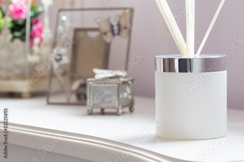 Reed diffuser with sticks in a frosted glass jar on a white sideboard with ornaments