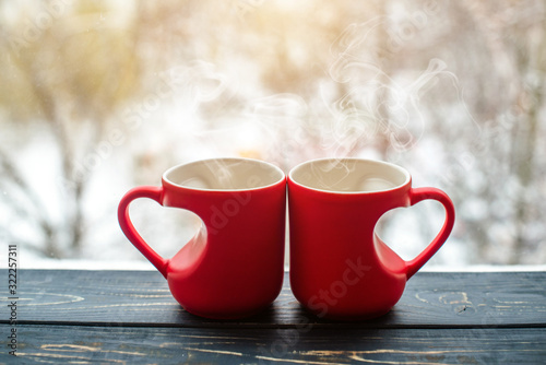 two heart shaped mugs with tea on the background of a window in winter