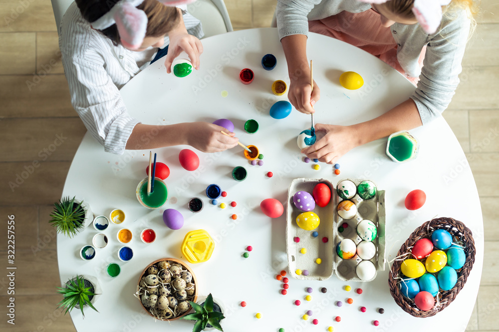 Top view, children at the table paint Easter eggs, paints, work atmosphere.