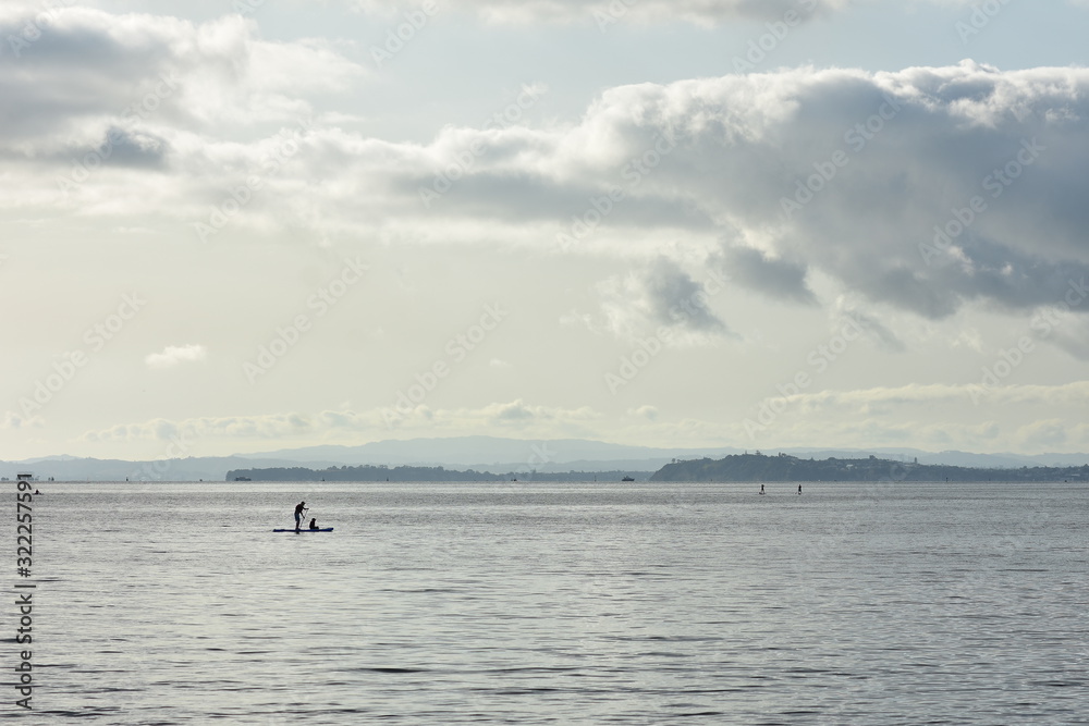 Fototapeta premium Paddleboarding na odległość na powierzchni dużego, bardzo spokojnego portu w tylnym świetle.