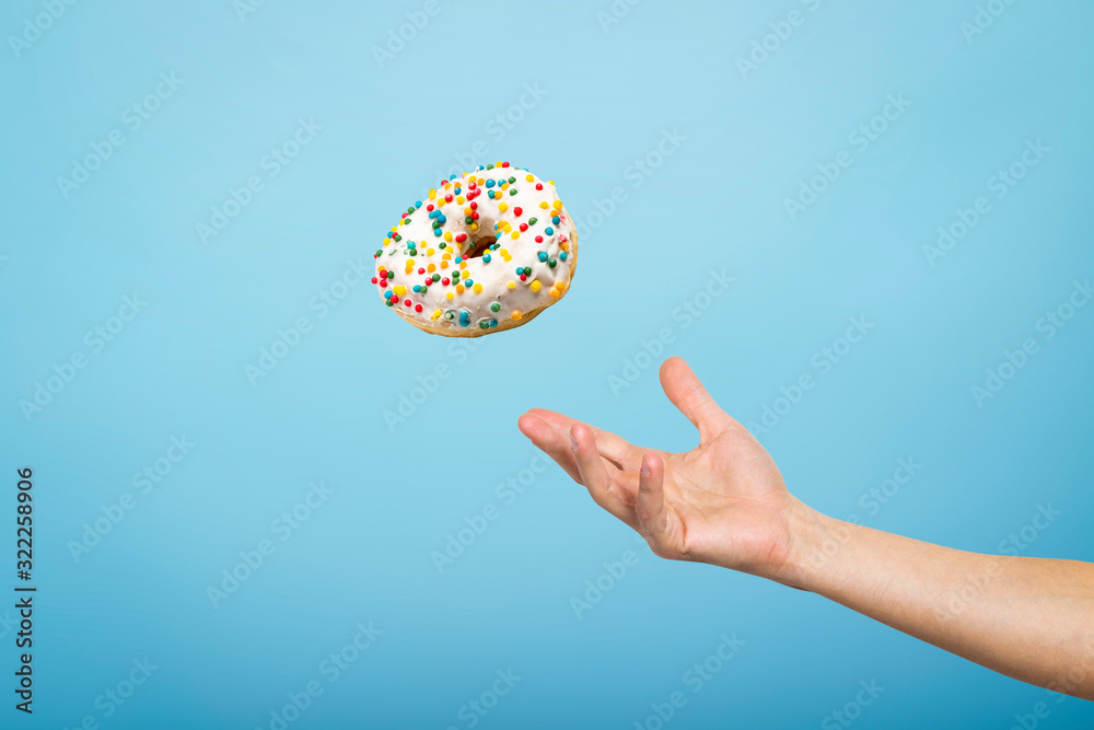 Hand catch a donut with icing. Blue cardboard background. Concept of baking, handmade. Flat lay, top view Hand catch a donut with icing. Blue cardboard background. Concept of baking, handmade. Flat lay, top view