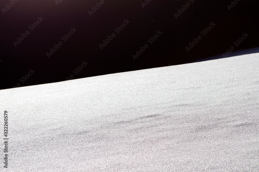 Snowy slope with textured surface with black background. Snow-covered surface with visible texture. Abstract winter background with contrast shadow.