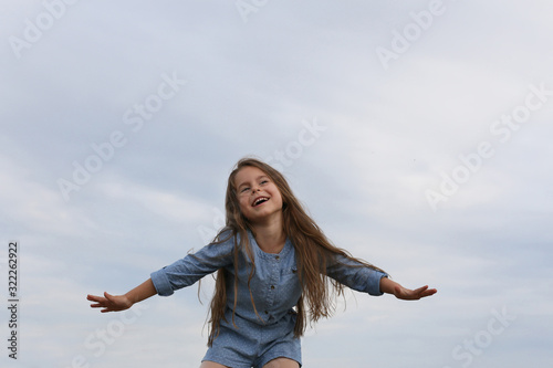 photo of a six year old girl laughing with arms wide open and her hair fluttering in the wind against a blue sky