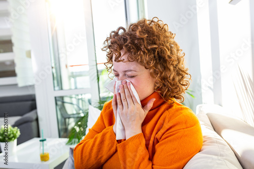 Sick desperate woman has flu. Rhinitis, cold, sickness, allergy concept. Pretty sick woman has runnning nose, rubs nose with handkerchief. Sneezing female. Brunette sneezing in a tissue