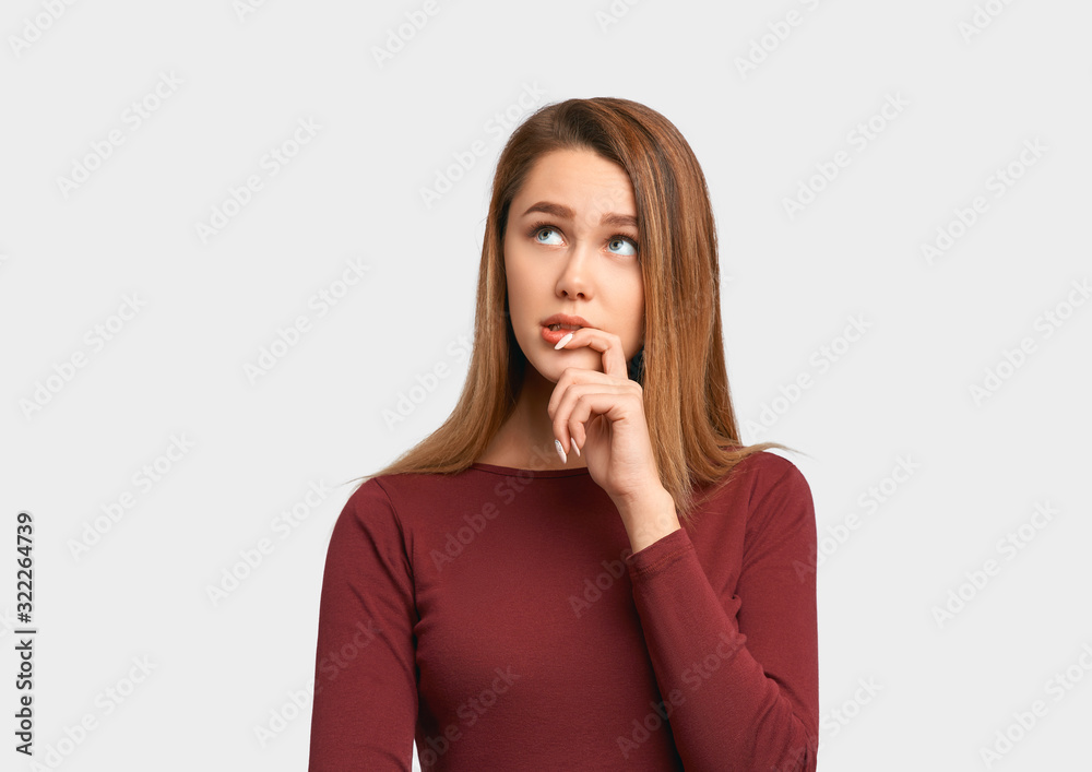 Photo girl looks with interest expression aside, keeps hand near lips. Beautiful young woman wears jacket sleeves isolated on white background in Studio with an empty space for text and advertising. Photo girl looks with interest expression aside, keeps hand near lips. Beautiful young woman wears jacket sleeves isolated on white background in Studio with an empty space for text and advertising.