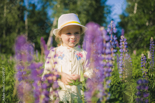 Portrait of a little girl in a hat in a field of flowers. Field of Lupins. Summer