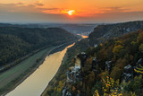 Saxon Switzerland with the Elbe valley in the evening. Landscape in the national park from the Bastei bridge with the Elbe and rocks, trees and forests in the autumn mood with an orange horizon at sun