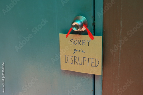 Closeup handwriting cardboard sign with message read sorry you are disrupted hanging on doorknob of wooden door, disruption concept 