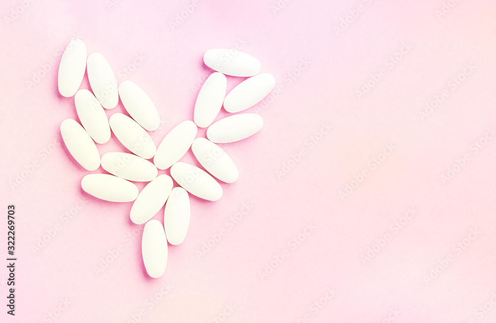 white heart from tablets and pills isolated on pink background with sunlight.