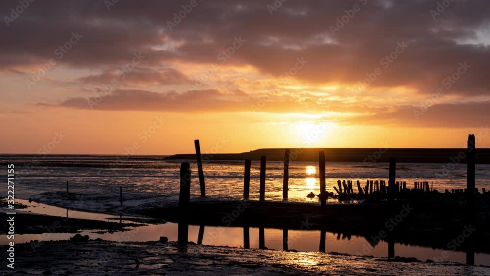 Sunrise time-lapse over mudflats, ocean and shoreline with wooden poles at texel Frisian wadden island Sunrise time-lapse over mudflats, ocean and shoreline with wooden poles at texel Frisian wadden island