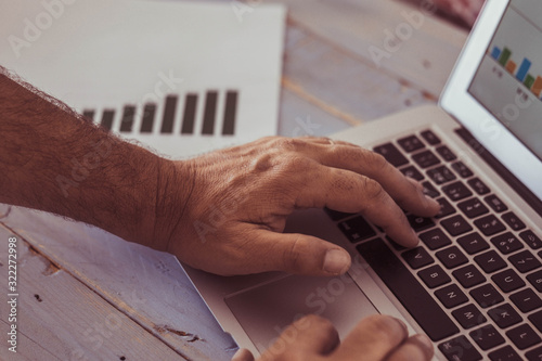 close up of hands of man typing in a laptop and looking ath the graphs on the screen and on the table - portrait or working man photo