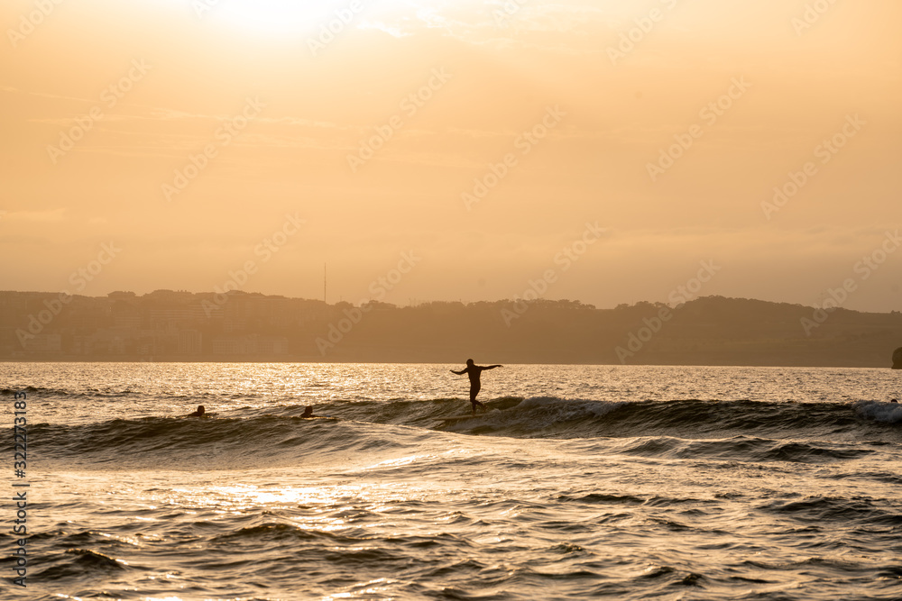 Wide image of surfers silhouettes surfing and riding waves at sunset o sunrise