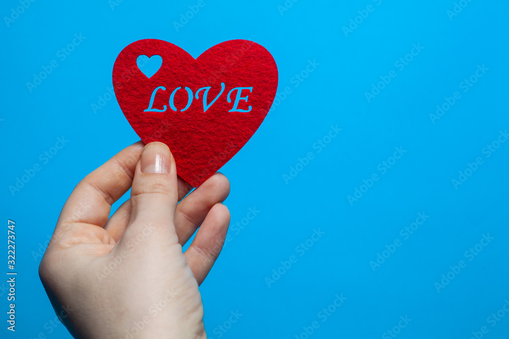 Fototapeta premium Decorative heart of red color with the inscription love in the hands of a man on a blue background
