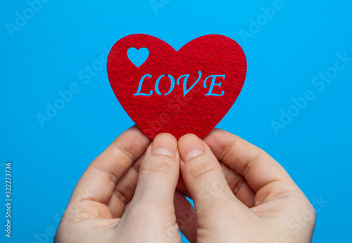 Decorative heart of red color with the inscription love in the hands of a man on a blue background
